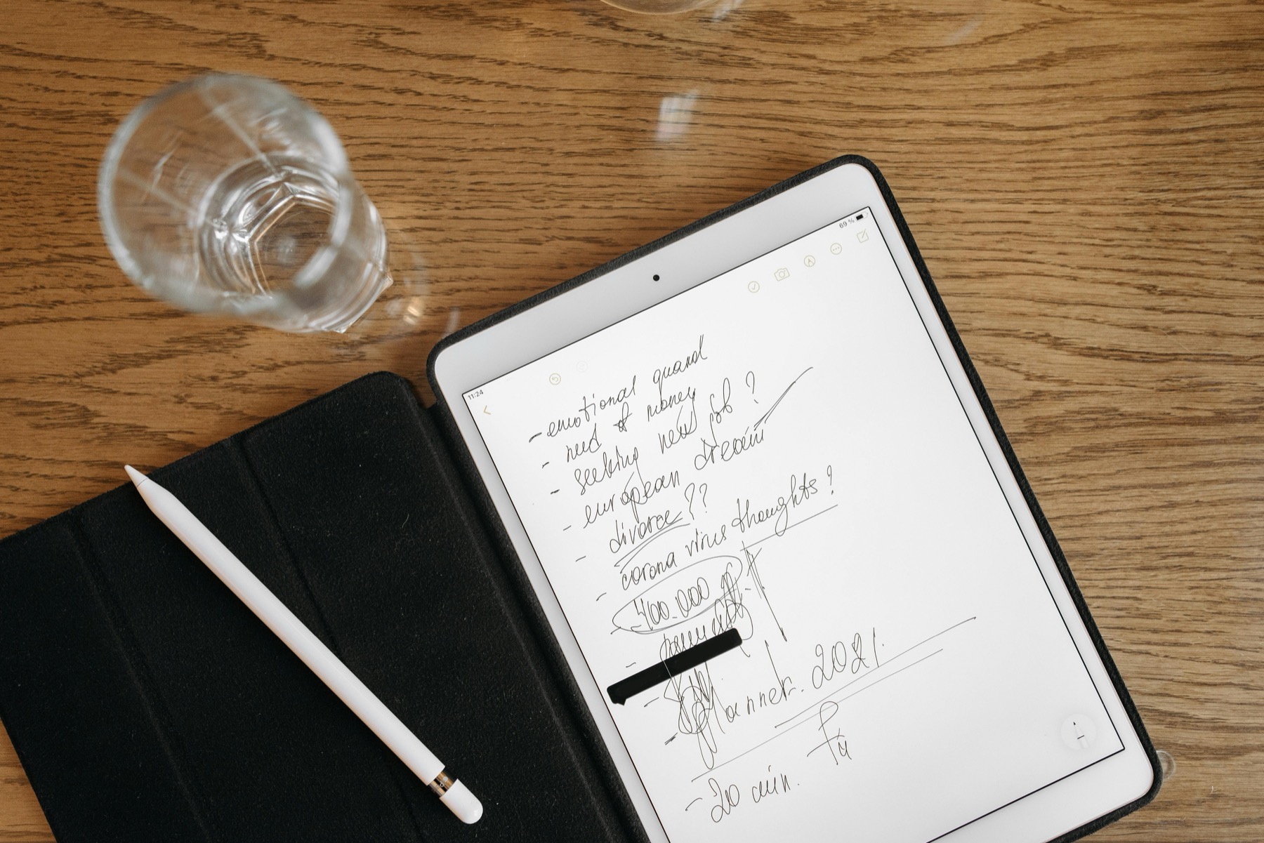 A tablet with handwritten notes and a stylus resting on a wooden desk beside a glass of water.